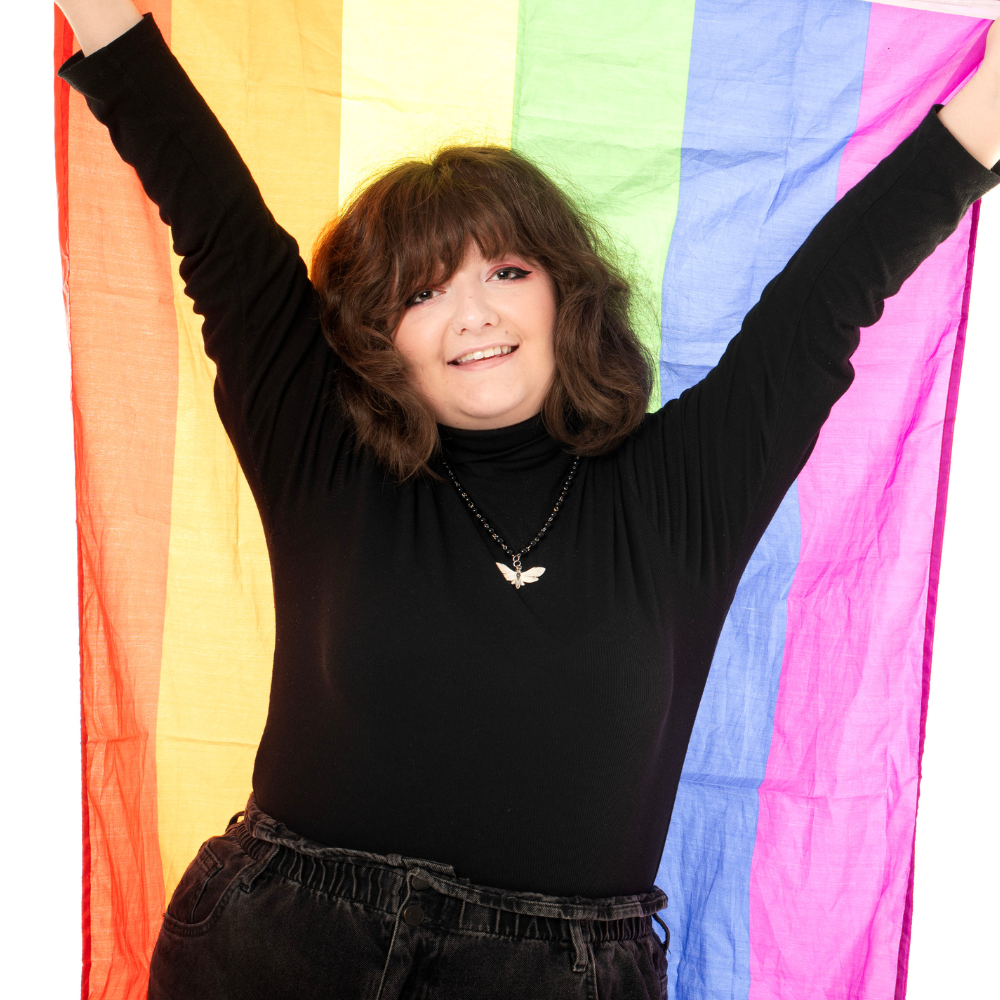 Leah Thompson, smiling and holding up a pride flag.